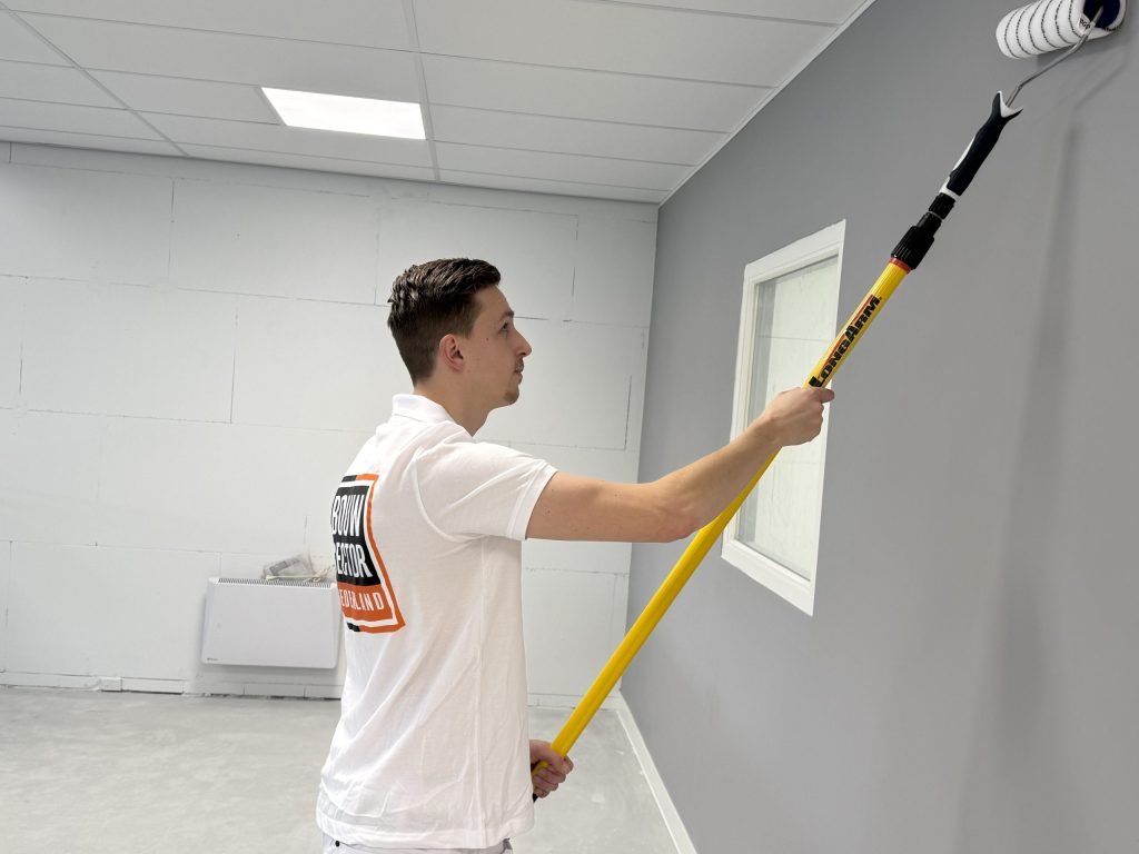 Schilder van Bouwsector Nederland rolt een grijze wand tot aan het plafond met een lange roller