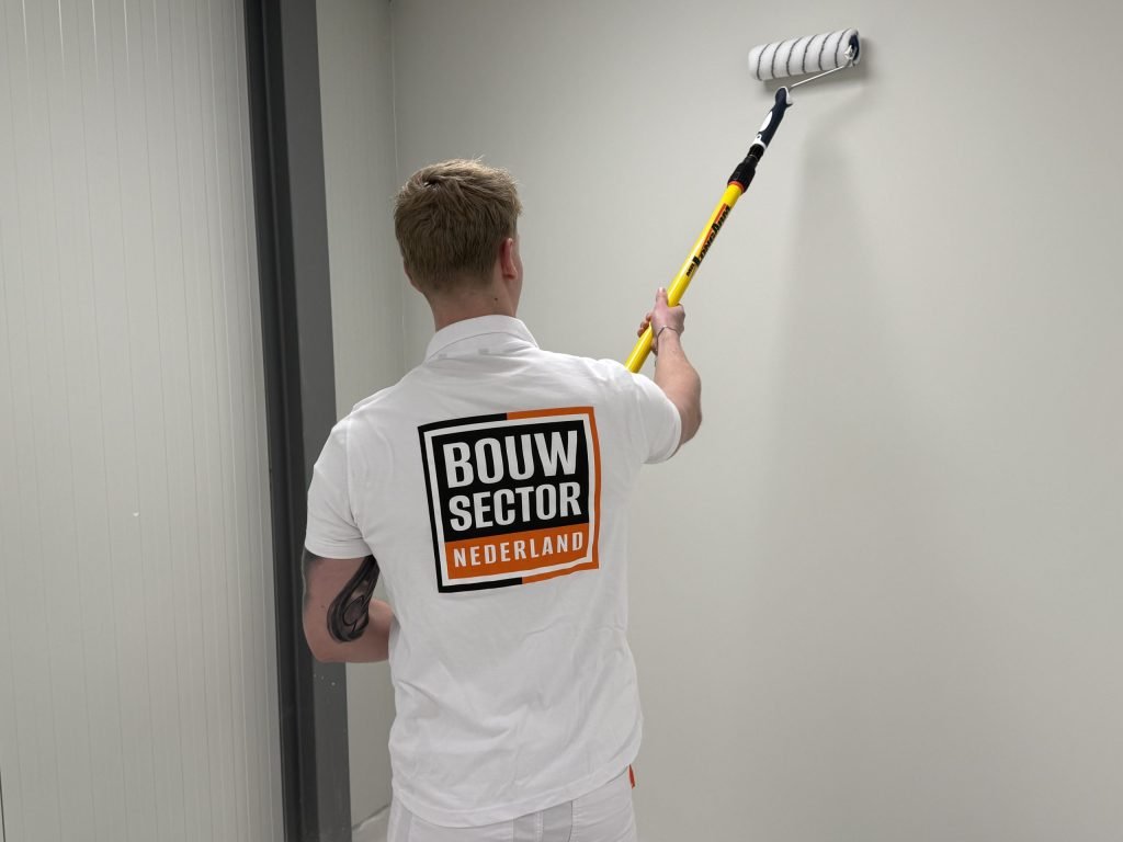 Schilder van Bouwsector Nederland in wit werkshirt rolt een lichte wand in een smalle ruimte