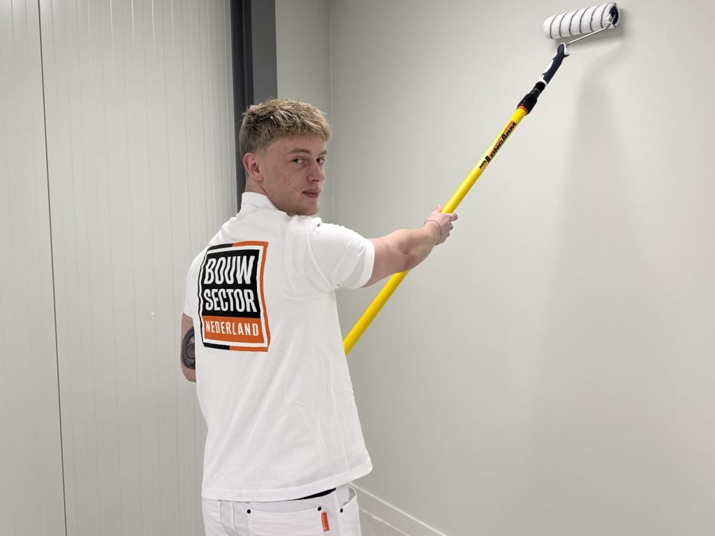 Schilder van Bouwsector Nederland kijkt om terwijl hij een lichte wand in een gang overschildert